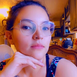 Headshot of person with dark hair in an updo, wearing cateye glasses and staring into the camera.